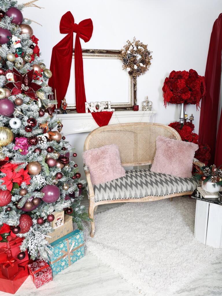 Christmas mini session backdrop in Vaughan with a cane settee, blush fur cushions, red roses and a burgundy decorated Christmas tree with wrapped gifts